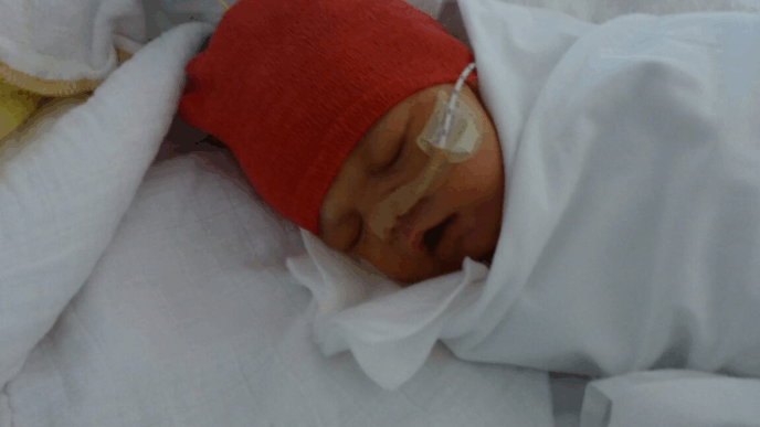 ziekenhuis met pasgeboren baby met rode muts met slang langs wang